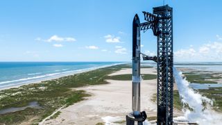 a huge silver rocket stands on a seaside launch pad