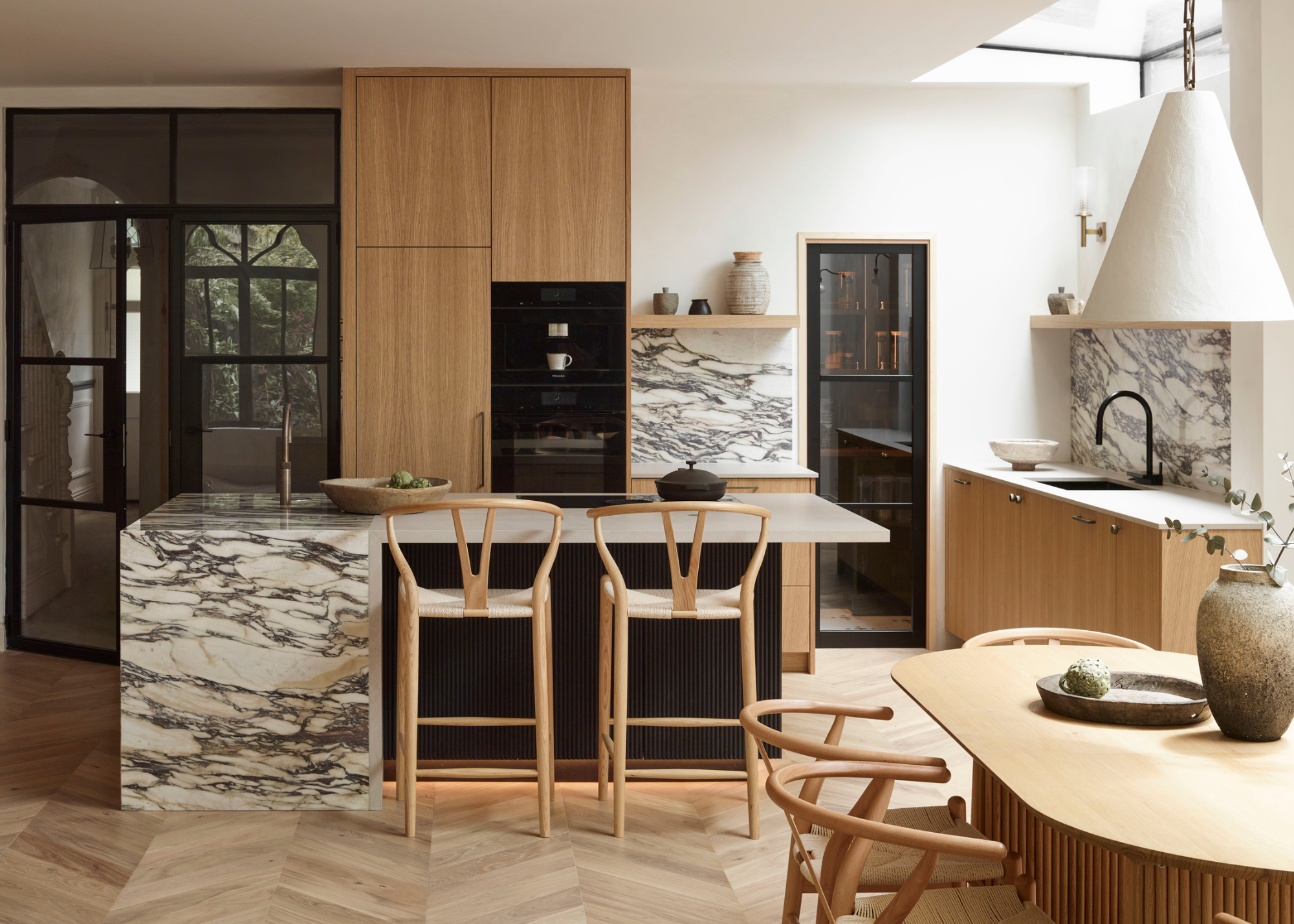 a wood and marble kitchen in an extension with an island in the middle and two bar stools beside it
