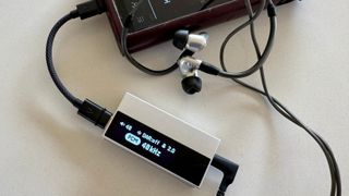 The Astell & Kern AK HC5 on a grey table, with the top plate illuminated and hooked up to Sennheiser IEMs and a FiiO digital audio player 