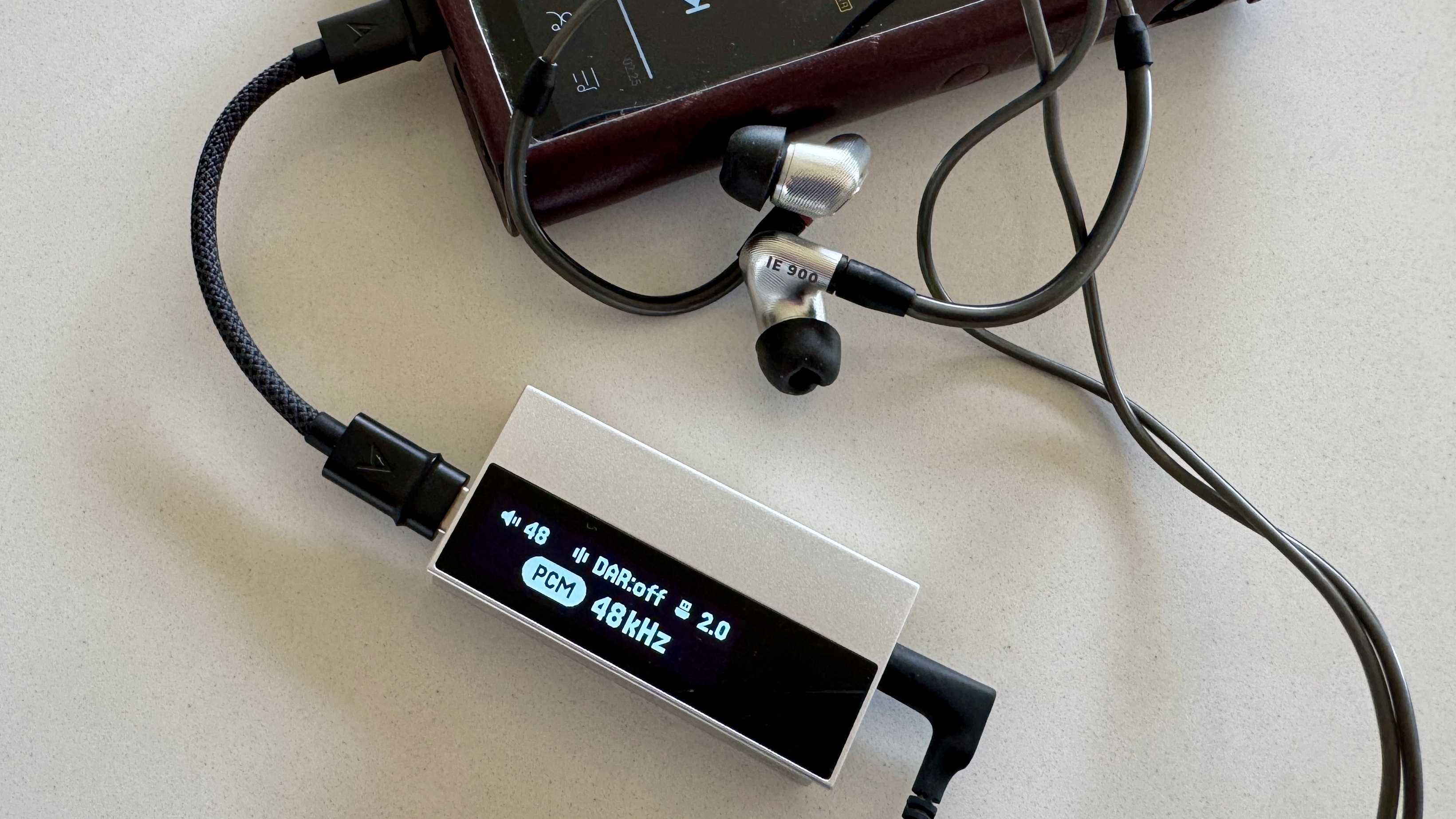 The Astell &amp; Kern AK HC5 on a grey table, with the top plate illuminated and hooked up to Sennheiser IEMs and a FiiO digital audio player 