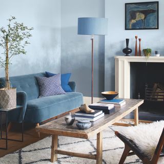 grey wall with lamp and sofa with cushions and books on wooden table