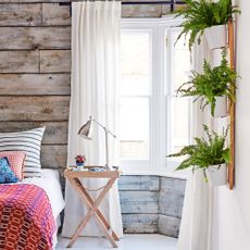 houseplants you should never place in a bedroom Wood panelled bedroom with sheer curtains, wooden bedside table and plants hanging from wall