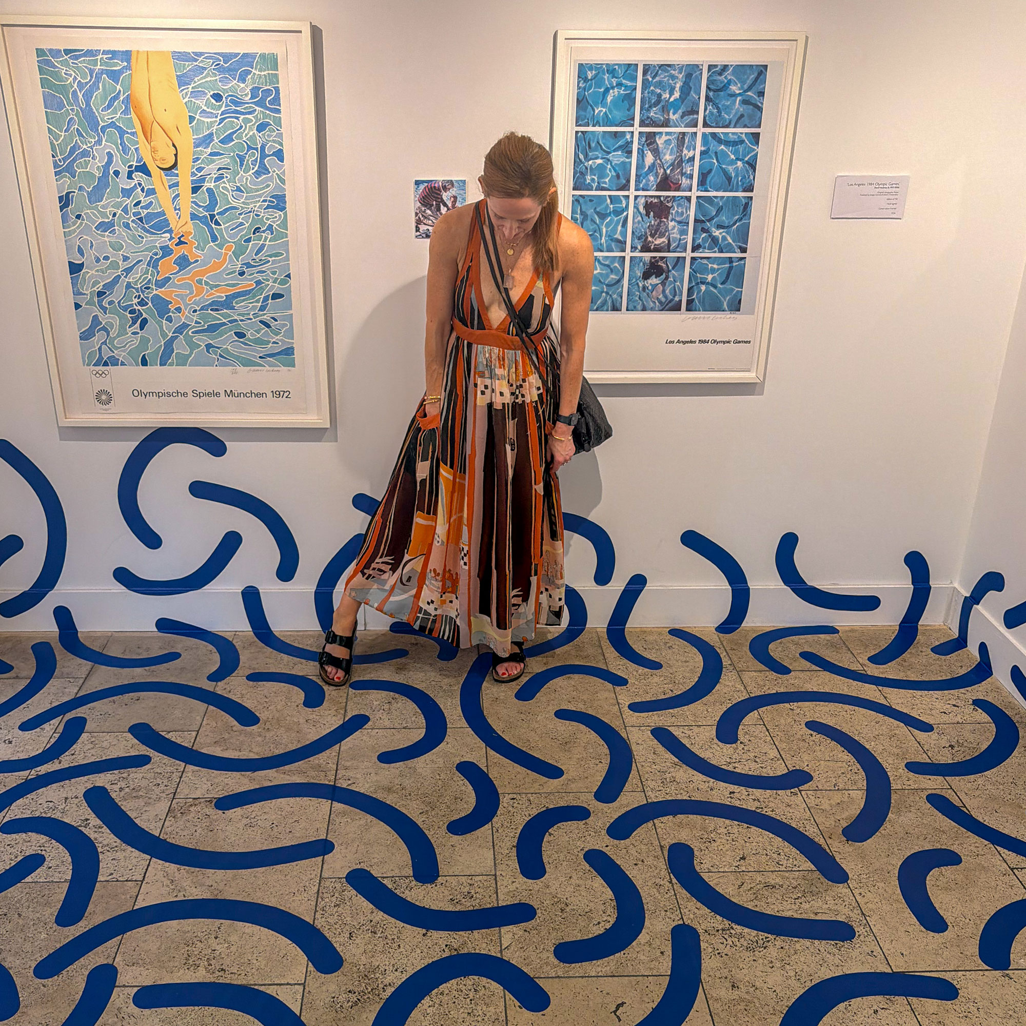Woman standing in art gallery looking down at floor covered in abstract blue squiggles