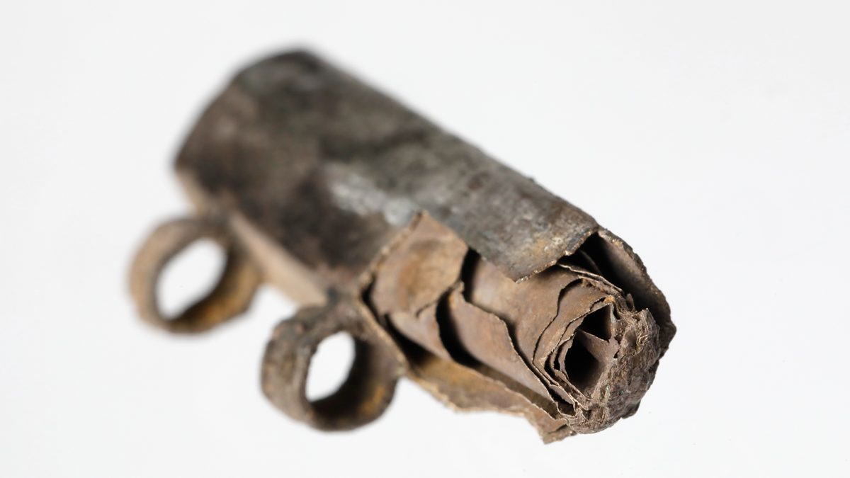 Silver amulet with rolled-up silver sheet inside against a white background