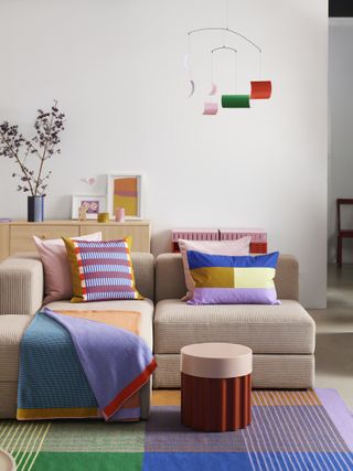 A living room with a neutral sofa and brightly colorfed soft furnishings