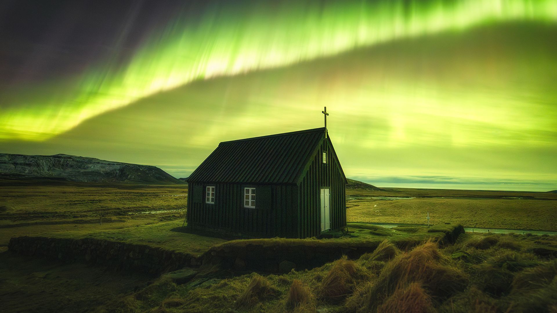 A house in the wilderness is seen below the green aurorae.