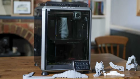 The Creality K1C on a table surrounded by dinoasaur 3D prints from our testing. A vase sits in the enclosure