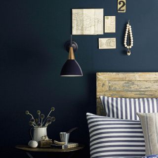 black and brass bedroom wall light with timber headboard and striped pillows