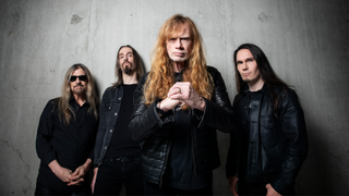 Megadeth standing against a grey backgroudn while Dave Mustaine holds his fist
