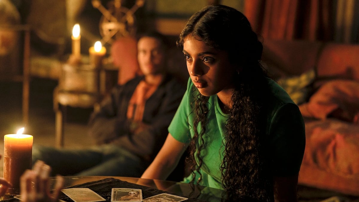 a woman (avantika) in a green shirt sits at a tarot table, with a man sitting in the background