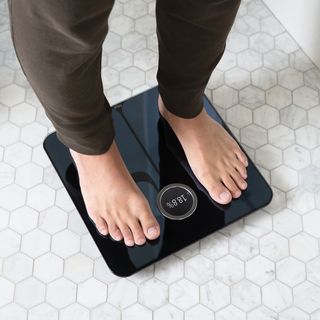 standing bare feet on a black digital Fitbit bathroom scale on white bathroom tiles