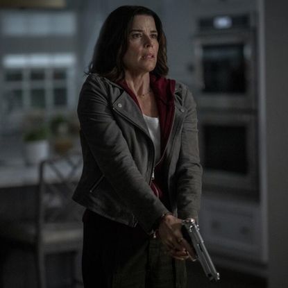 neve campbell as sidney prescott holding a gun looking scared in a dark house in scream 7