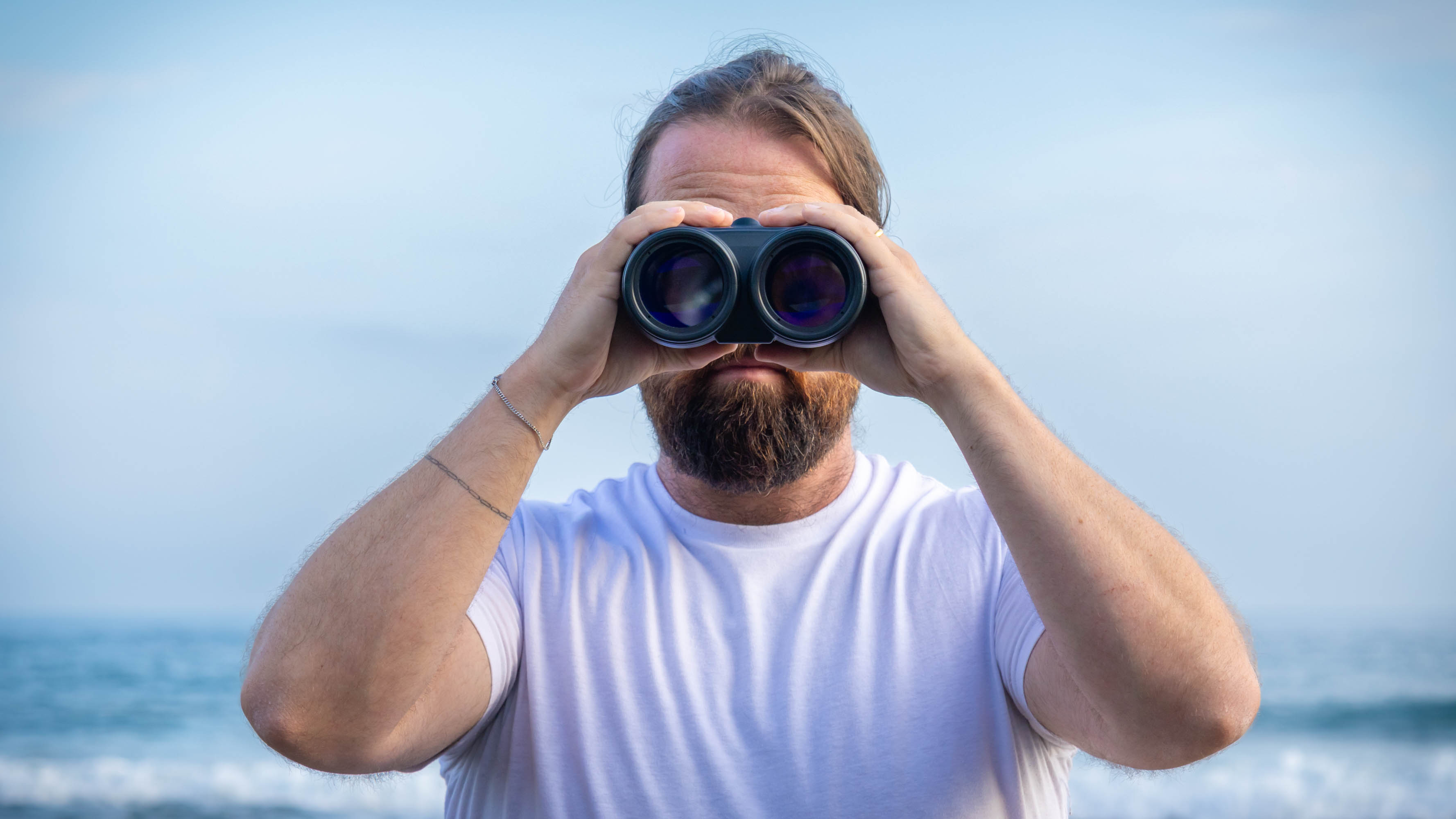A male using the Canon 18x50 IS binoculars, facing the camera with the sea behind them.
