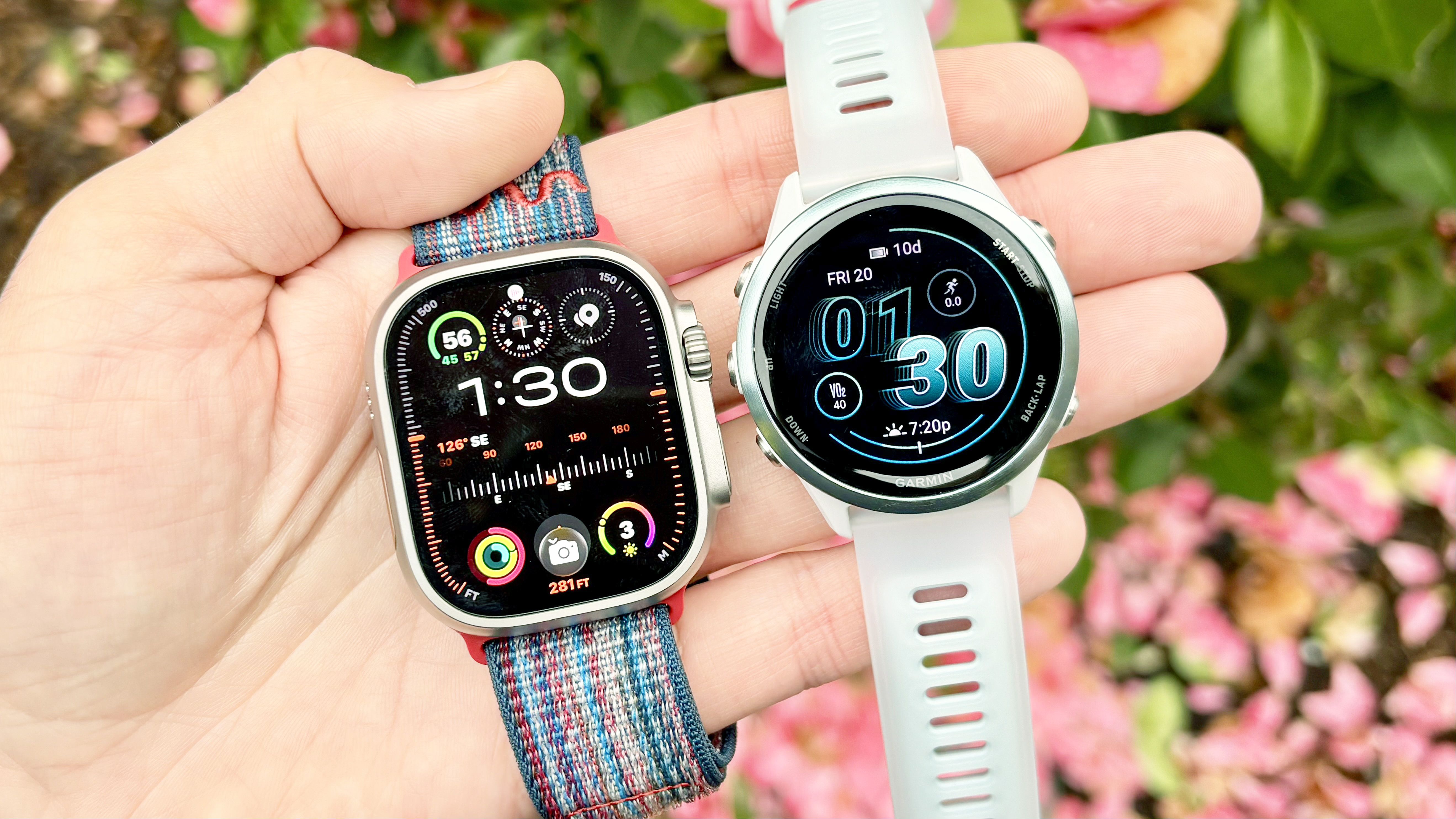 Close-up of the Apple Watch Ultra 3 and Garmin Forerunner 570 in a user's hand with blooming flowers in the background