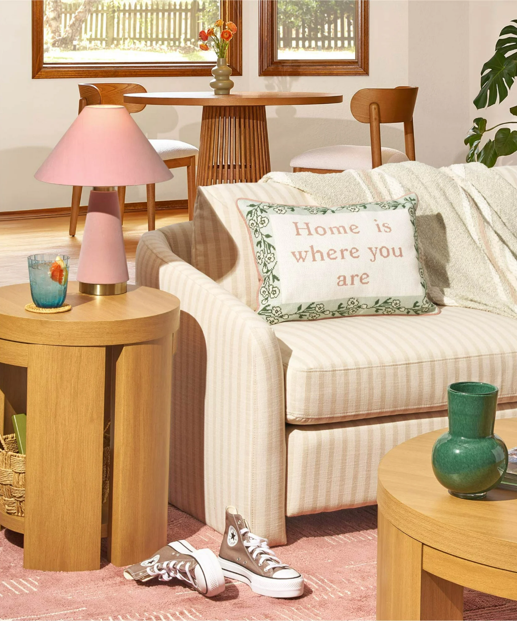 a living room with a small accent table with a pink lamp on it, a striped couch, a decorative pillow, and a coffee table with a green vase on it
