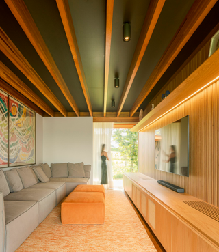 A living space with an L shaped grey sofa, wall paintings, two orange poofs, a side board, with an exposed ceiling structure