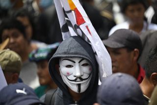 A close up of a hooded person wearing a Guy Fawkes mask in a crowd
