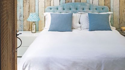 Double panelled bedroom with blue headboard, white bedding, blue cushions, white nightstand and gold lamp with blue and white patterned lampshade