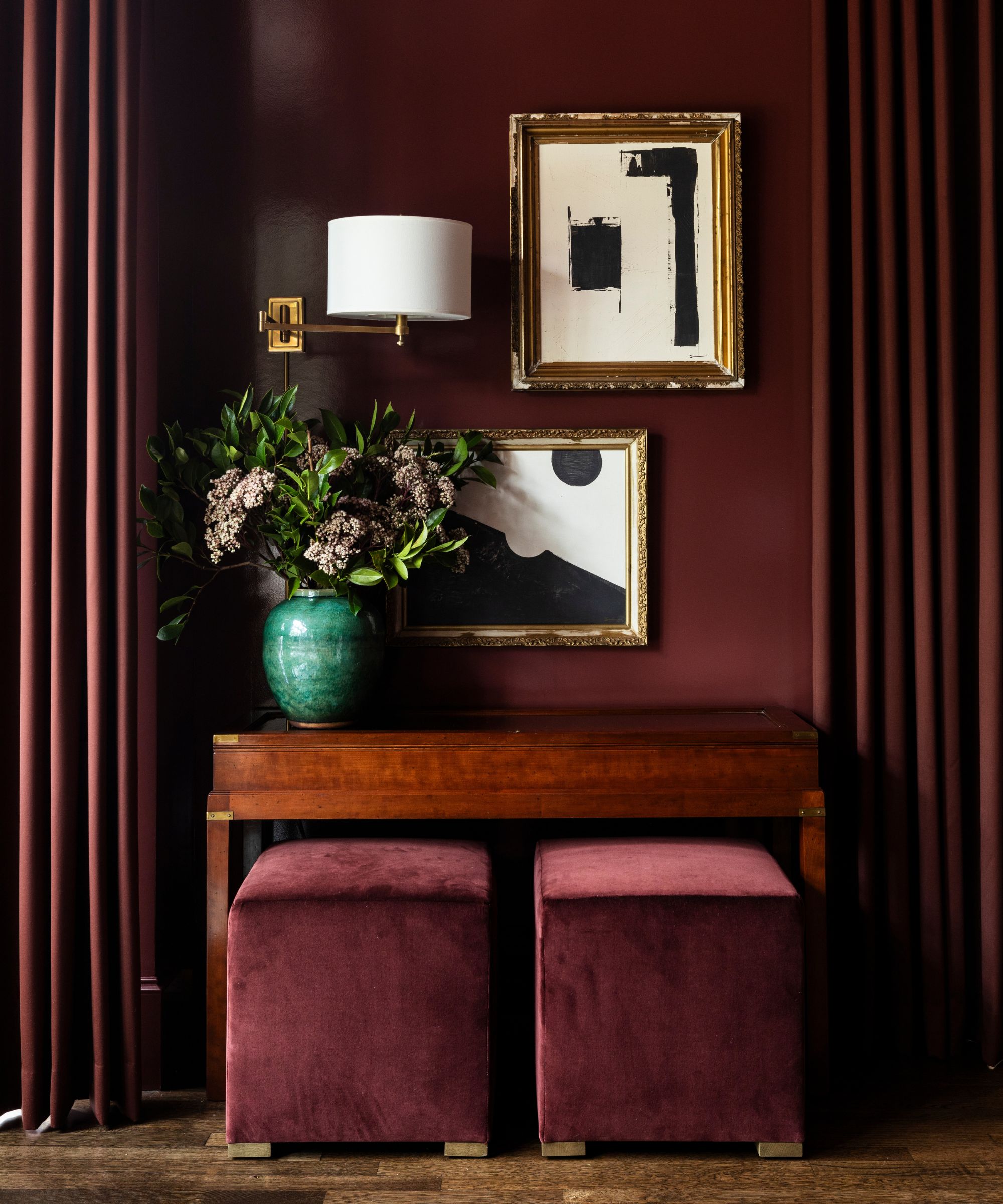 A corner of a color-drenched red room with a gallery wall, dark red curtains, and a wooden vanity with red seating.