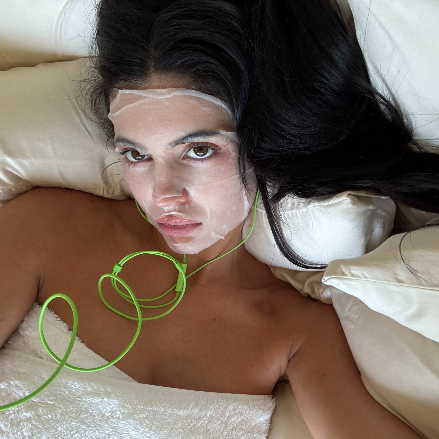Selfie of Kylie Jenner wearing a sheet mask and green headphones