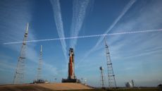 A large orange and white rocket sits on a launch pad with streaks of white clouds behind it