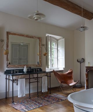 Neutral bathroom, wood flooring, vintage double washbasin counter, rug on floor, leather butterfly chair