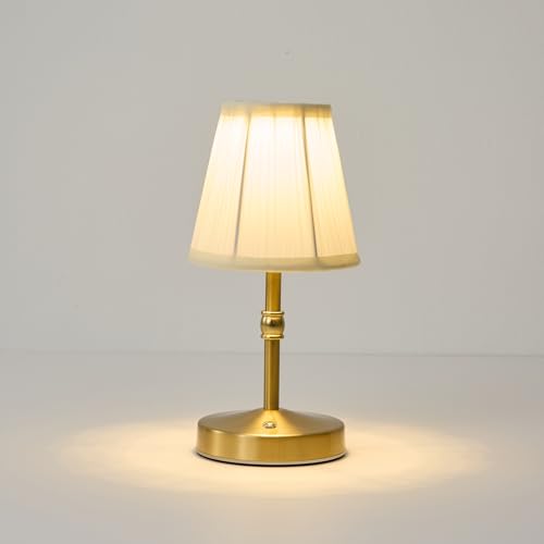 Mini, golden, cordless lamp, illuminated on white floor in front of white background.
