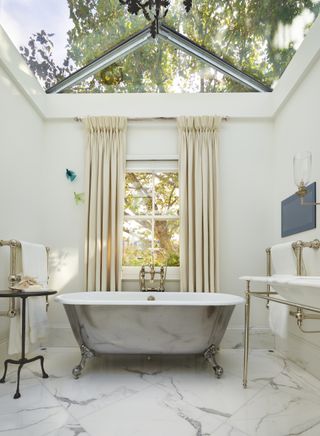 bathroom with skylight and window, marble floor and freestanding metallic bath in center