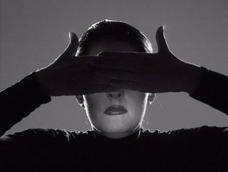 Marina Abramovic has her gloved hands over her eyes. The photo is black & white.
