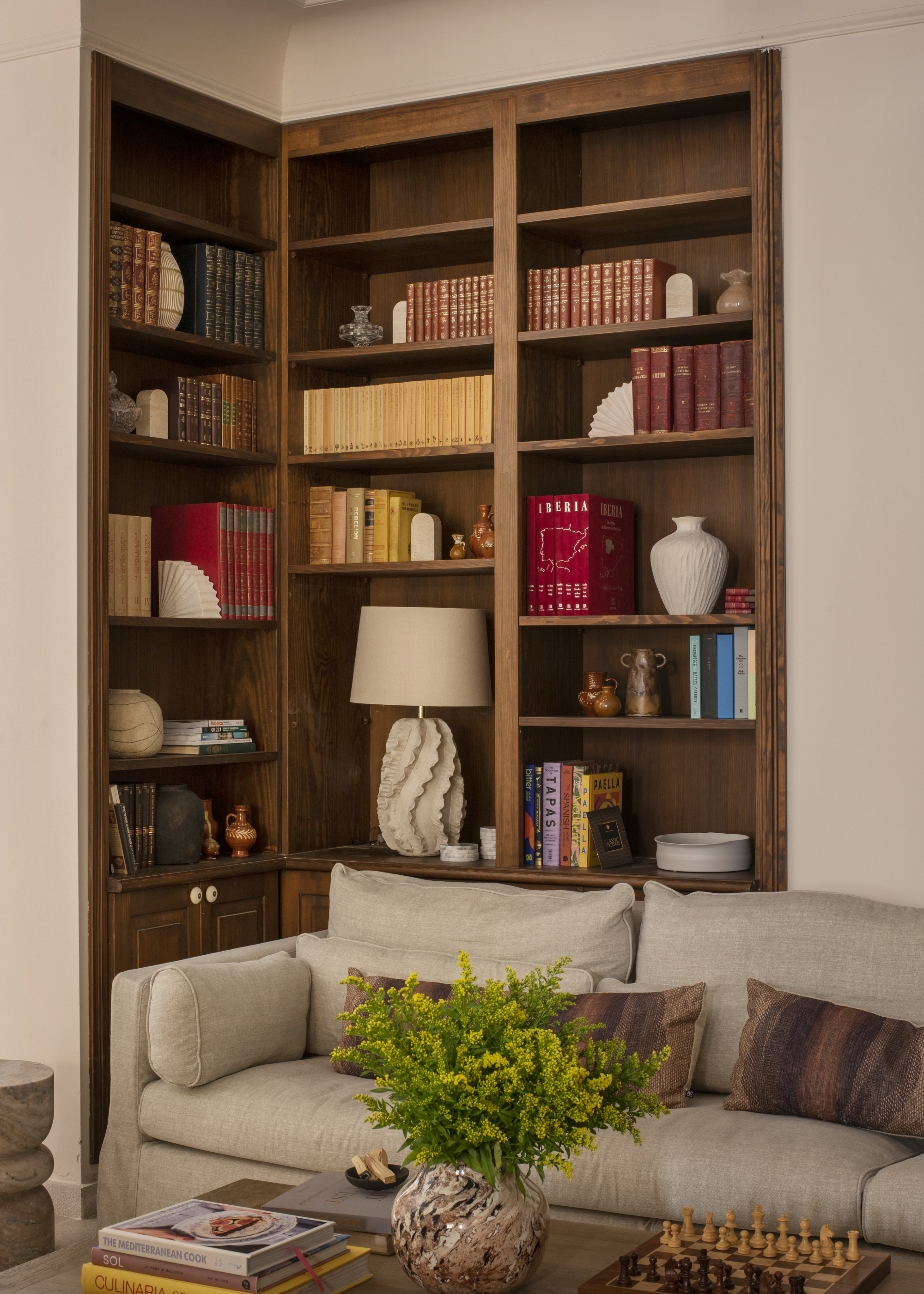 A living room with built-in corner bookshelves and a table lamp on one of the shelves