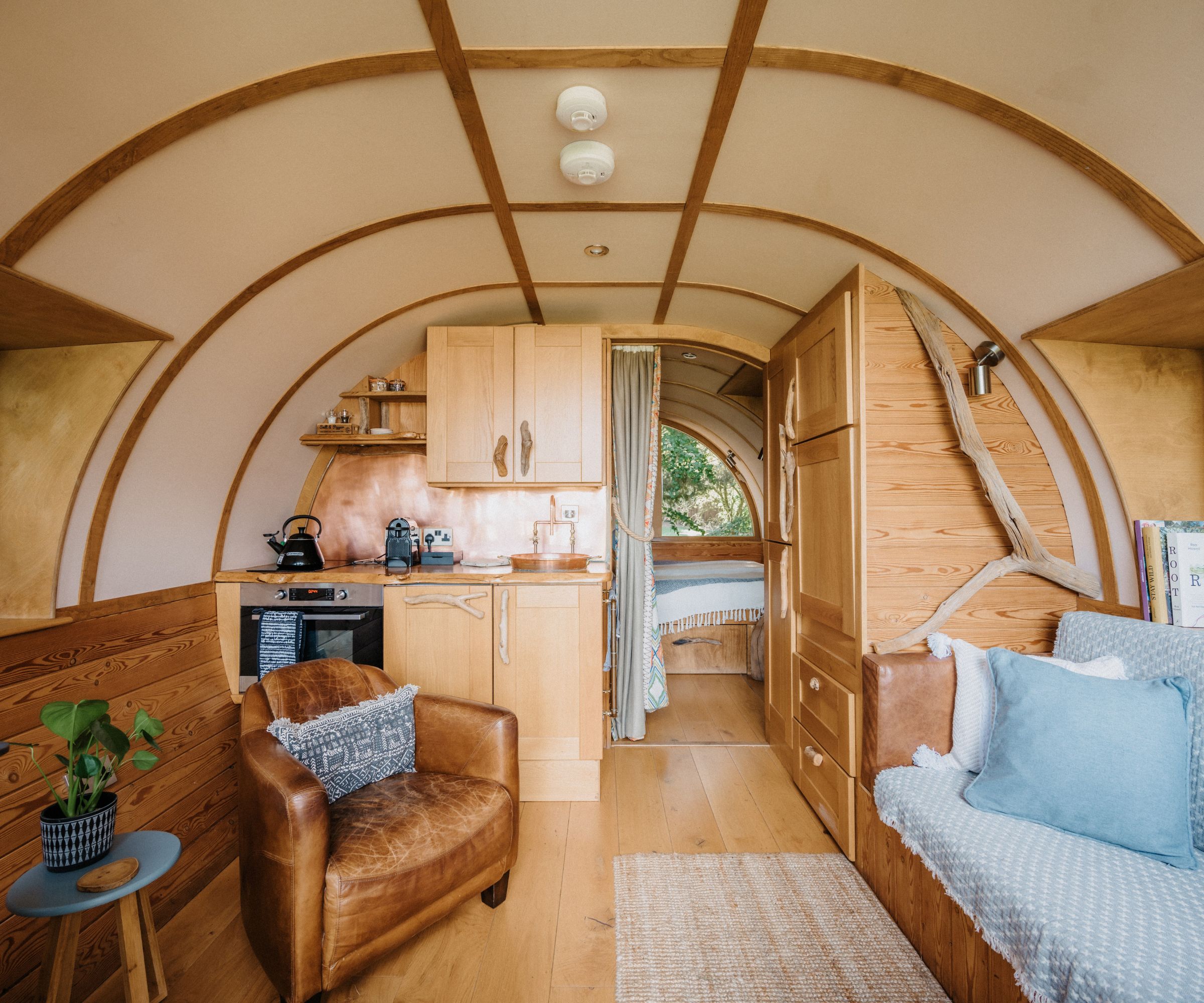 Cosy treehouse interior with curved timber walls, compact kitchen and soft seating in natural wood tones