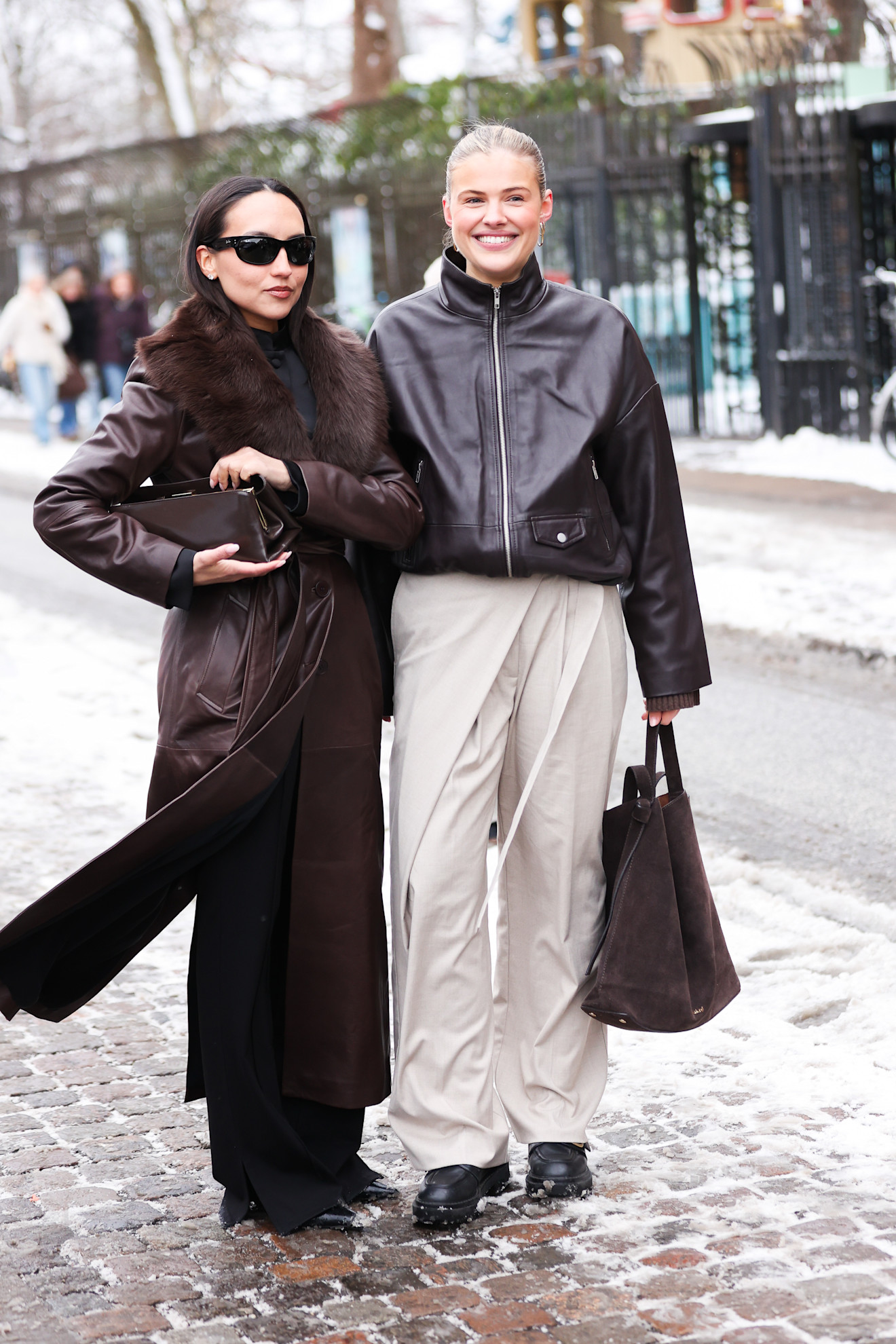 woman wearing brown jacket and brown pants; woman wearing leather jacket and white pants