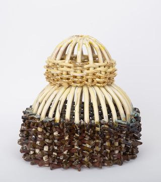 A headpiece-shaped ceramic piece features earthy tones and jewelry-like golden elements.