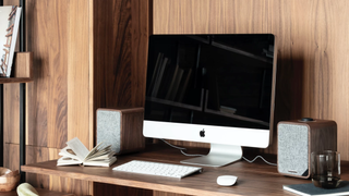 Ruark MR1 Mk2 speakers flanking an Apple Mac desktop screen in a wood-background home office setting