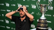 Angel Hidalgo puts his hands on top of his head while sitting next to the Open de Espana trophy