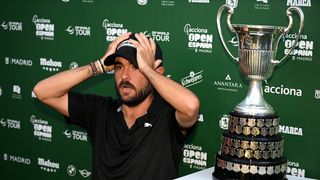 Angel Hidalgo puts his hands on top of his head while sitting next to the Open de Espana trophy