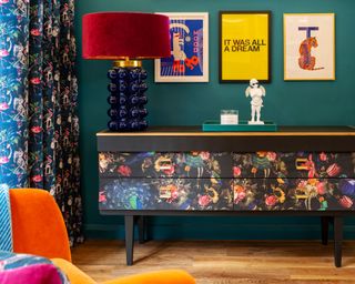 Eclectic lounge with teal wall, colorful gallery wall, bobble retro lamp, and pattern clashing on sideboard and curtain.