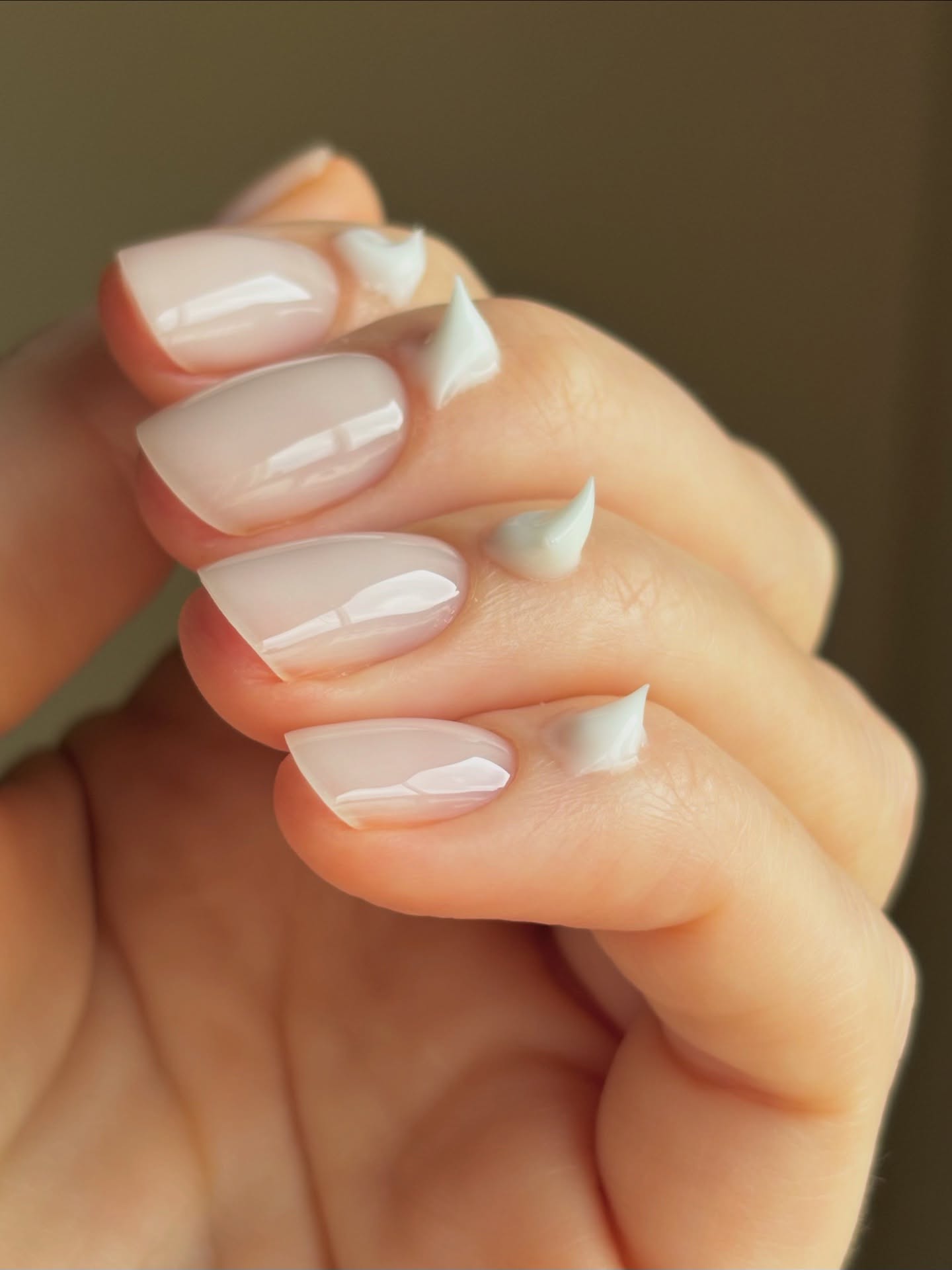A photo of short nails painted with a sheer pink polish with cuticle cream applied at the base of each nails