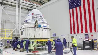 People in blue lab coats working on Boeing&#039;s blue and white Starliner spacecraft