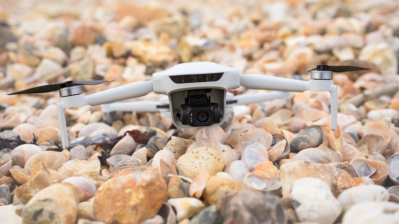Potensic Atom 3 beginner drone in flight on a pebble beach ahead of take off