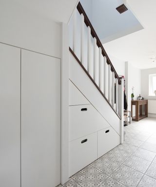 An image of a white stair case with wooden hand rails and under stair pull-out storage boxes
