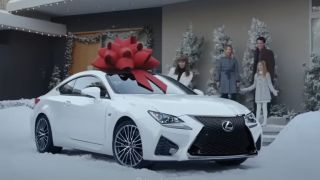 A Lexus with a giant red bow on top of it and a family in the background.