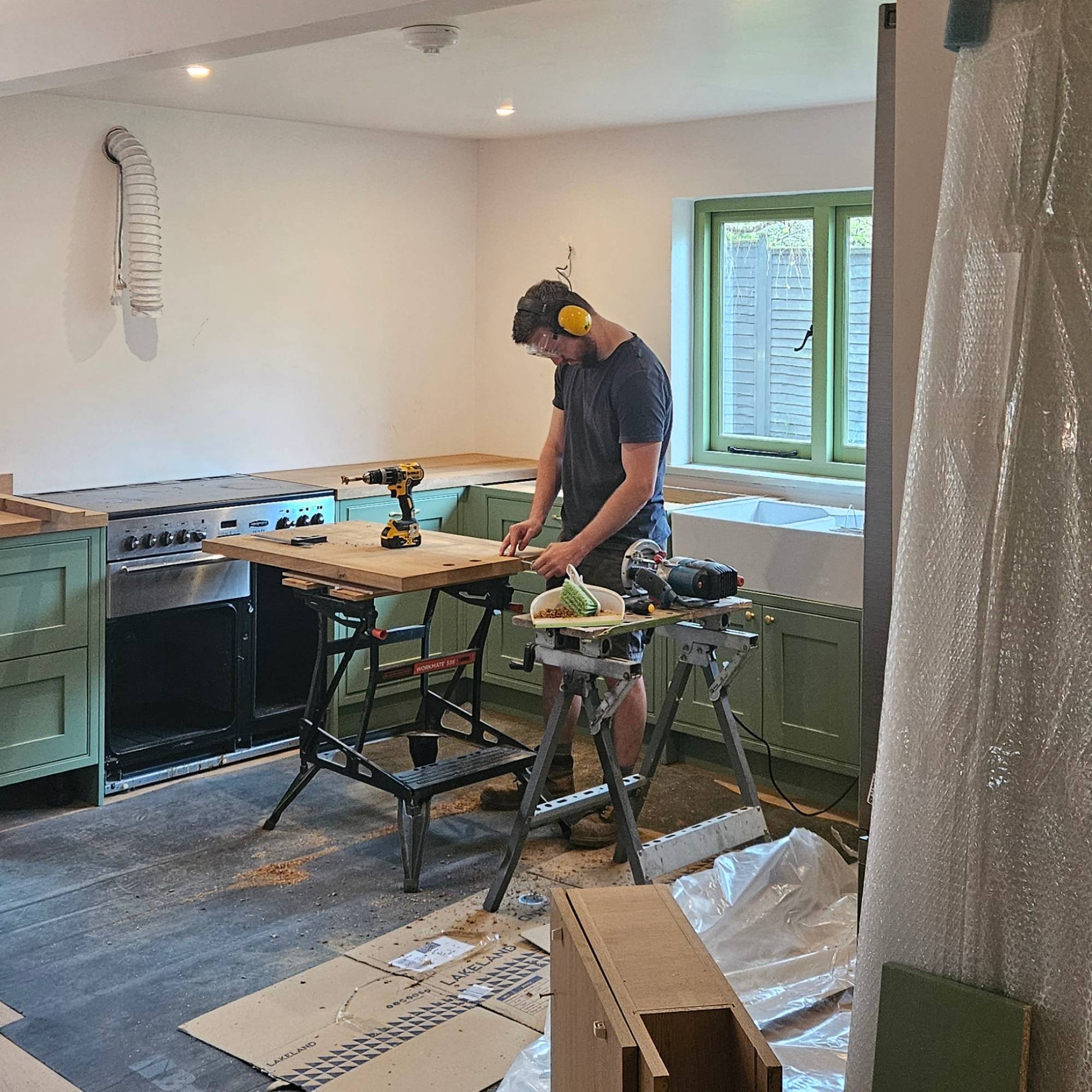 green kitchen being installed by man with ear defenders on