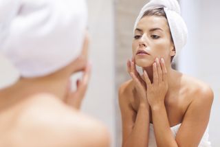 A woman looks closely at her skin in a mirror.