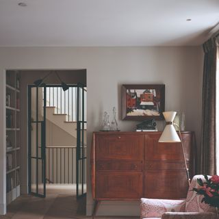 A living room with a beige wall, downlights installed into the ceiling and a floor lamp over a patterned armchair