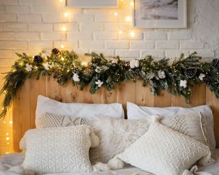 a scandinavian bedroom with a christmas garland and lights above the wooden headboard