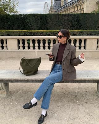 A French woman wearing a brown sweater and blazer with jeans.