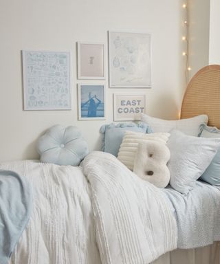 Relaxed bedroom with white painted walls, textured, bamboo style bedframe, white bedding, patterned cushion and pastel throw, brass wall light, wall art mounted above, wooden side table, taupe painted trim on wall