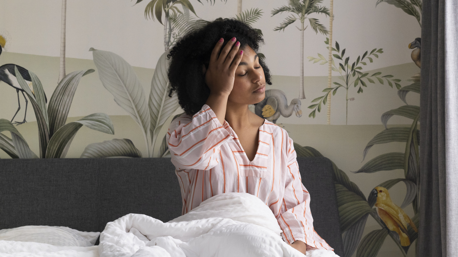 Woman sitting up in bed with her palm on her forehead and her eyes closed