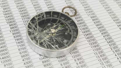 A smashed compass on top of financial paperwork.